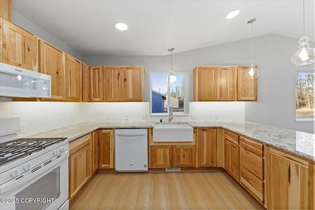 kitchen with a sink, white appliances, light wood finished floors, lofted ceiling, and light stone countertops