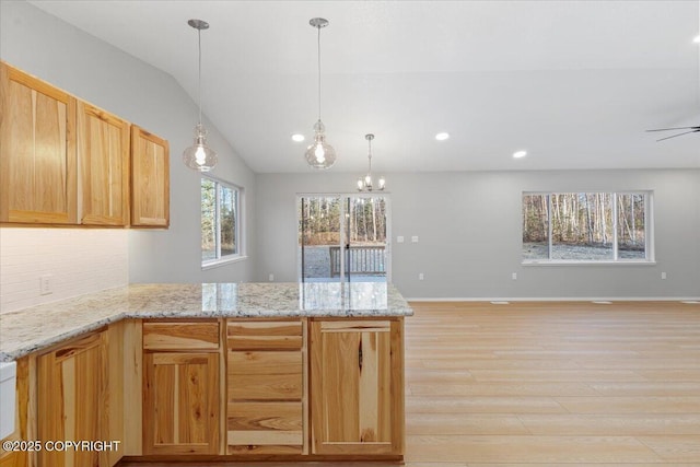 kitchen featuring light stone countertops, light wood finished floors, a peninsula, hanging light fixtures, and vaulted ceiling