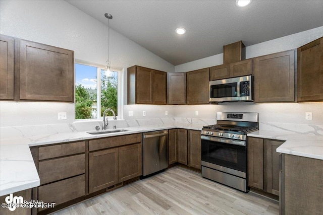 kitchen featuring a sink, light stone counters, decorative light fixtures, stainless steel appliances, and vaulted ceiling