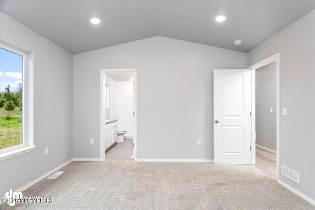 unfurnished bedroom with visible vents, light colored carpet, connected bathroom, and lofted ceiling