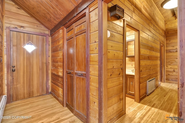 corridor with light wood-style floors, wooden walls, wooden ceiling, a baseboard radiator, and lofted ceiling