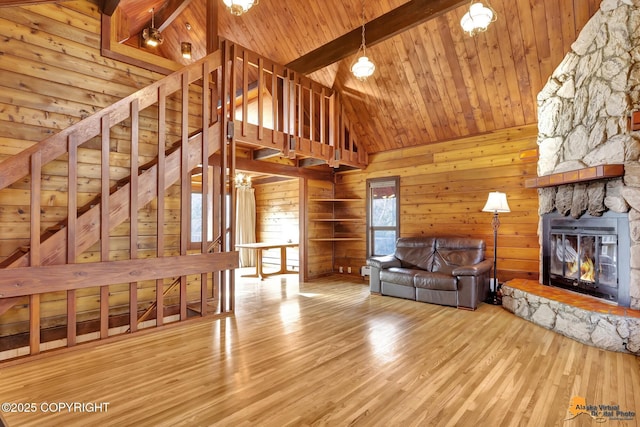 unfurnished living room featuring beam ceiling, wood finished floors, a stone fireplace, wood walls, and wood ceiling