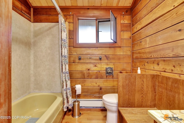 full bath featuring wood finished floors, a baseboard radiator, shower / bath combo with shower curtain, wood walls, and toilet