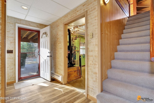 entrance foyer with stairs, a drop ceiling, wood finished floors, and brick wall