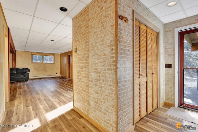 hall featuring a drop ceiling, wood finished floors, brick wall, and a baseboard radiator