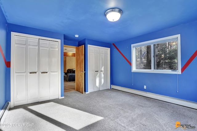 unfurnished bedroom featuring a baseboard heating unit, two closets, and carpet flooring