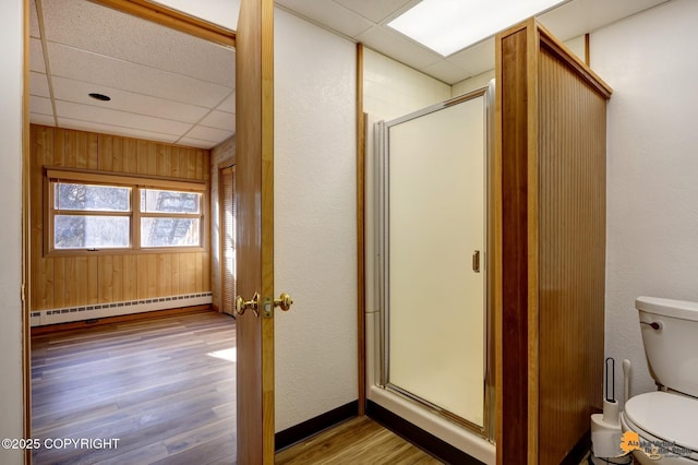 full bathroom with a shower stall, wood finished floors, a drop ceiling, and a baseboard radiator