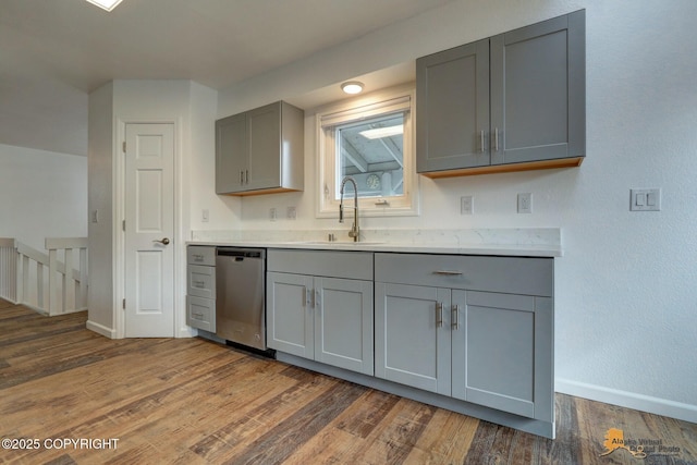 kitchen featuring gray cabinetry, dishwasher, a sink, baseboards, and wood finished floors