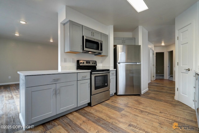 kitchen with stainless steel appliances, gray cabinets, light wood-type flooring, baseboards, and light countertops