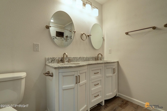 bathroom featuring wood finished floors, toilet, double vanity, a shower, and baseboards