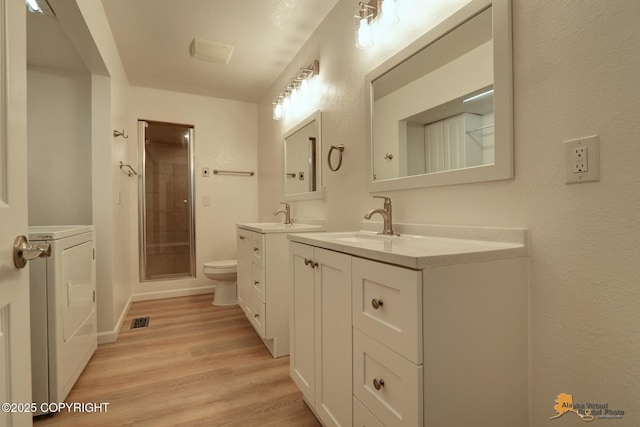 full bath featuring washer / dryer, wood finished floors, a shower stall, two vanities, and toilet