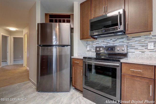 kitchen with stainless steel appliances, tasteful backsplash, baseboards, brown cabinets, and light stone counters