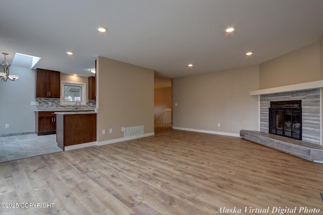 unfurnished living room featuring light wood finished floors, baseboards, a tiled fireplace, and recessed lighting
