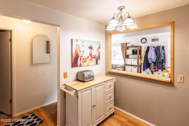 hallway with a notable chandelier, light wood-type flooring, baseboards, and a textured wall