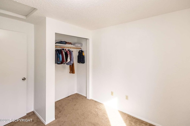 unfurnished bedroom with a closet, a textured ceiling, attic access, and carpet flooring