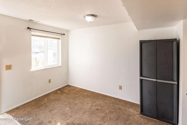 carpeted spare room featuring baseboards, visible vents, and a textured ceiling