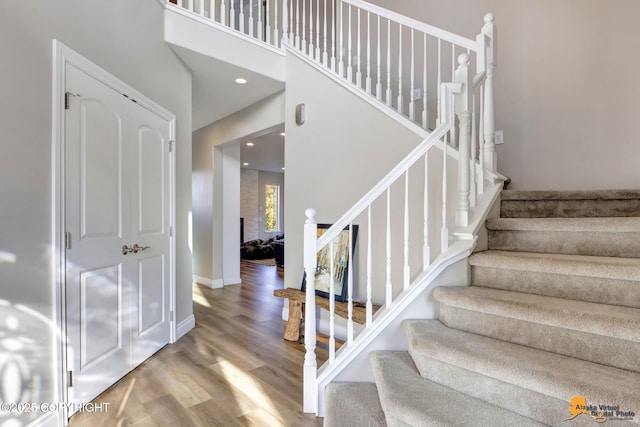 staircase with recessed lighting, baseboards, a high ceiling, and wood finished floors