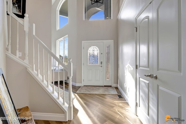 entryway featuring visible vents, stairway, light wood finished floors, baseboards, and a towering ceiling