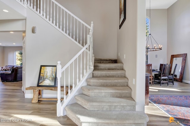 staircase featuring recessed lighting, an inviting chandelier, wood finished floors, and a towering ceiling