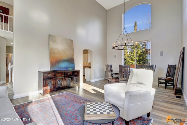 living area with arched walkways, an inviting chandelier, wood finished floors, and a towering ceiling