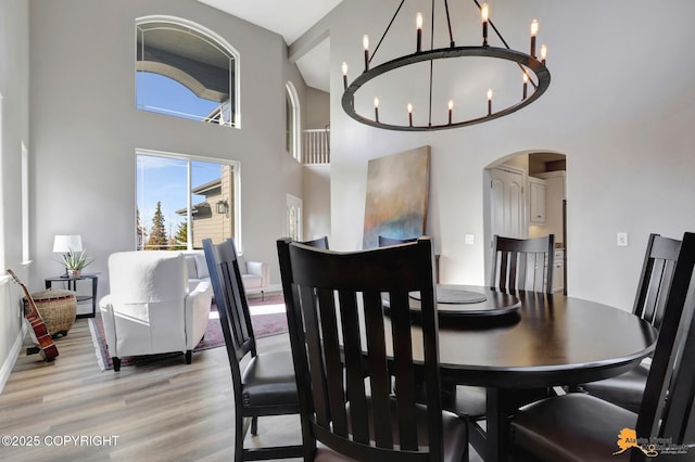 dining area with arched walkways, an inviting chandelier, a high ceiling, and light wood-style floors