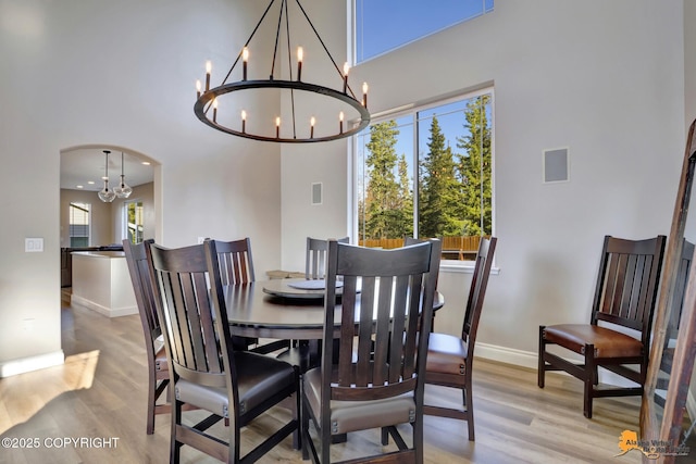 dining space with baseboards, light wood-type flooring, arched walkways, and a healthy amount of sunlight