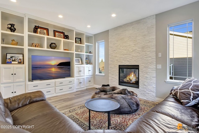 living area with a stone fireplace, recessed lighting, baseboards, and wood finished floors