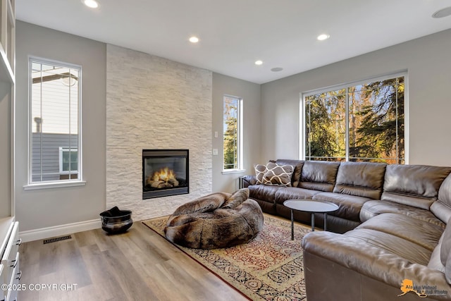 living area featuring recessed lighting, visible vents, a stone fireplace, and wood finished floors