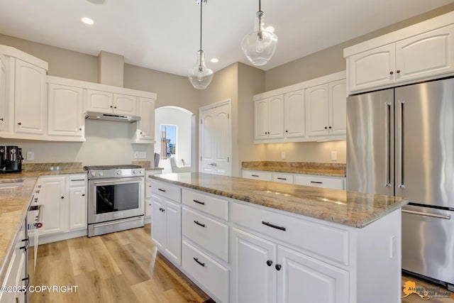 kitchen featuring a kitchen island, under cabinet range hood, light stone counters, appliances with stainless steel finishes, and arched walkways