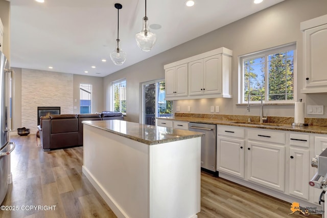 kitchen with light wood finished floors, a fireplace, stainless steel dishwasher, stone countertops, and a sink