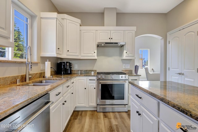 kitchen featuring stone counters, arched walkways, a sink, under cabinet range hood, and appliances with stainless steel finishes