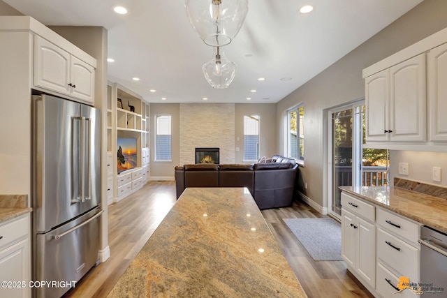 kitchen with light stone counters, light wood-style flooring, white cabinets, high quality fridge, and a large fireplace