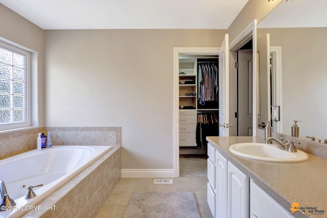 bathroom with vanity, a tub with jets, visible vents, a walk in closet, and tile patterned floors