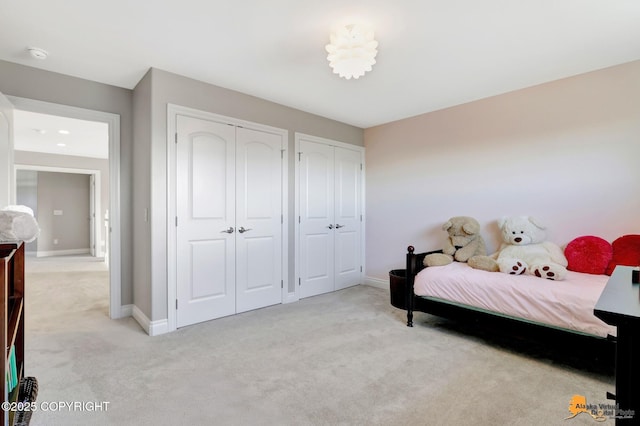 bedroom featuring light colored carpet, baseboards, and two closets