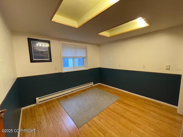 spare room with a baseboard heating unit, baseboards, and wood finished floors