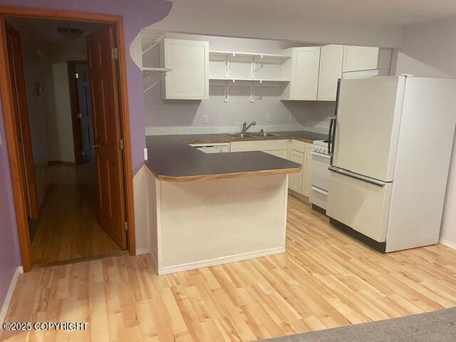 kitchen with dark countertops, a peninsula, light wood-style floors, white appliances, and a sink