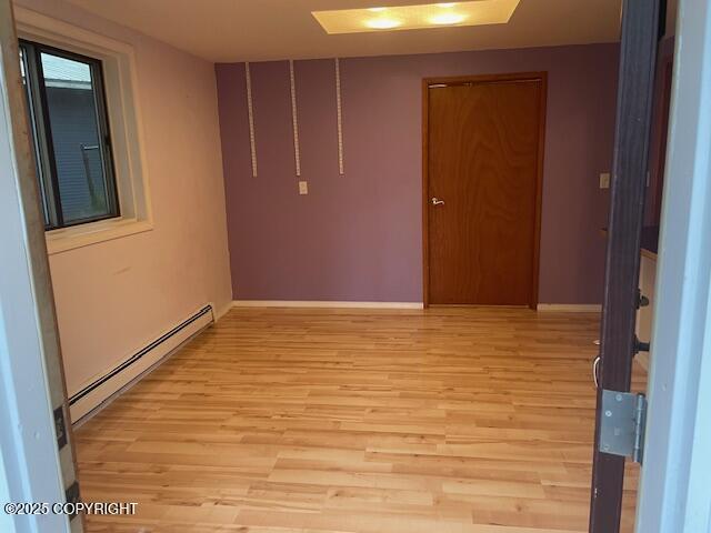 unfurnished room with light wood-style floors, baseboards, and a baseboard radiator