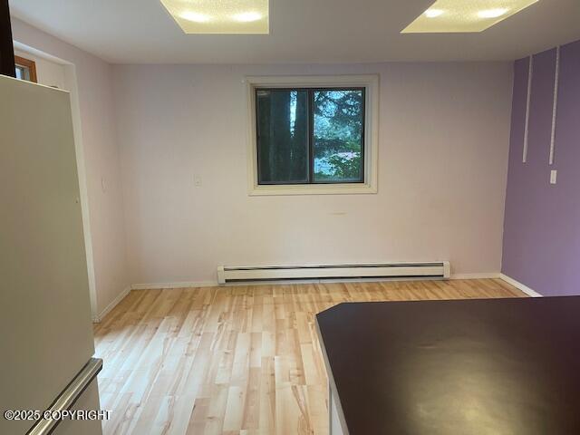 spare room featuring a baseboard heating unit, baseboards, and light wood finished floors