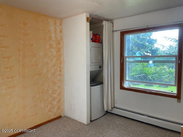 unfurnished room featuring a wealth of natural light, stacked washer / drying machine, and baseboard heating