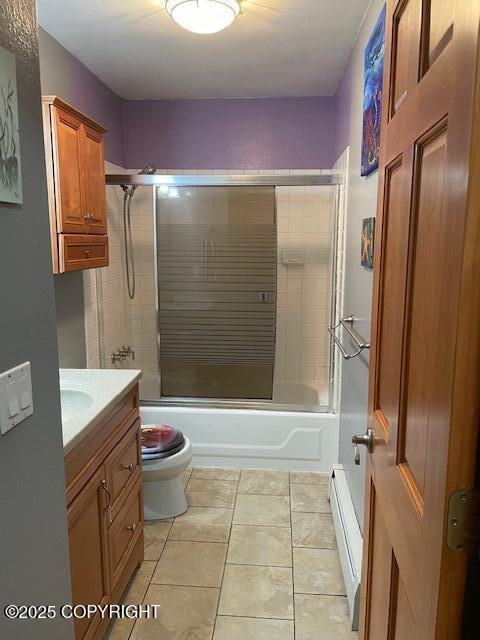 full bath featuring vanity, bath / shower combo with glass door, tile patterned flooring, a baseboard heating unit, and toilet