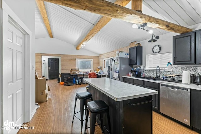 kitchen featuring vaulted ceiling with beams, a sink, appliances with stainless steel finishes, a kitchen bar, and light wood-type flooring