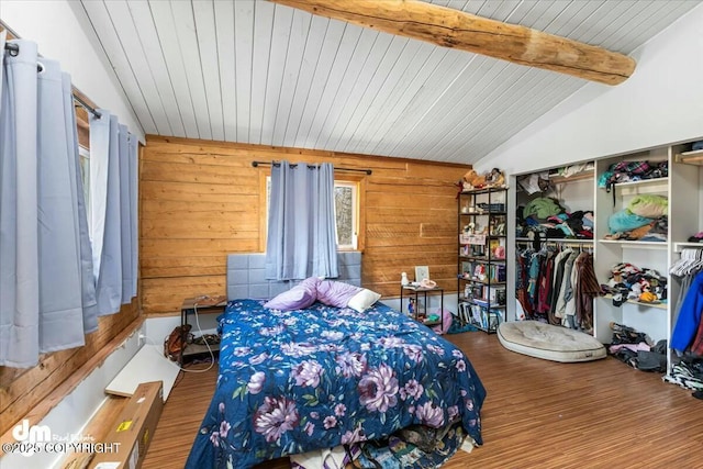 bedroom featuring a closet, wooden walls, vaulted ceiling with beams, and wood finished floors