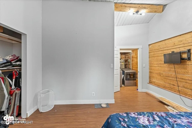 bedroom featuring beam ceiling, washer / clothes dryer, wood finished floors, a closet, and baseboards