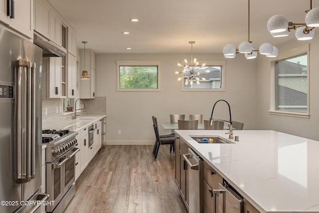 9475 E Spring Creek Cir, Wasilla, AK 99654 - kitchen with high end appliances, a sink, light wood-style floors, a chandelier, and light stone countertops