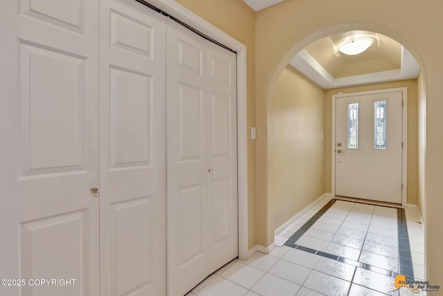 entrance foyer with arched walkways, light tile patterned floors, a tray ceiling, and baseboards