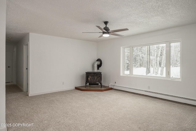 unfurnished living room with a baseboard heating unit, a textured ceiling, carpet, ceiling fan, and a wood stove