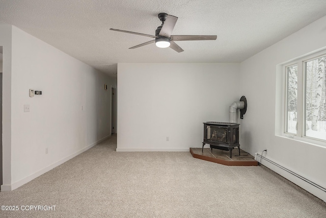 unfurnished living room featuring ceiling fan, carpet, baseboard heating, a wood stove, and a textured ceiling