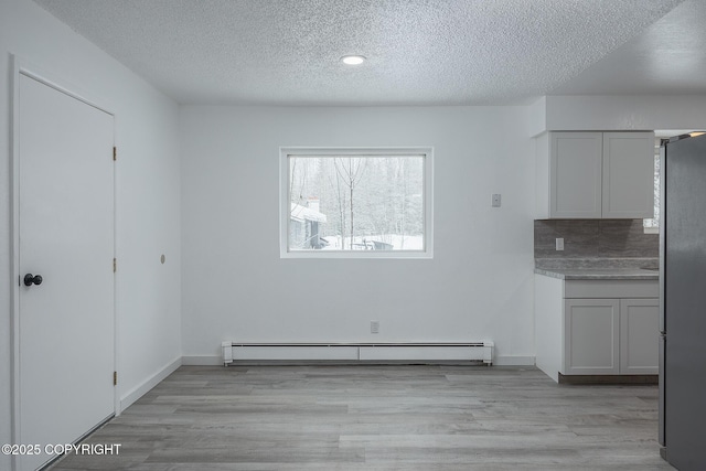 unfurnished dining area with a baseboard radiator, baseboards, a textured ceiling, and light wood-style flooring