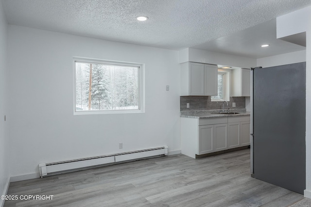 kitchen featuring light wood finished floors, a sink, decorative backsplash, white cabinets, and baseboard heating