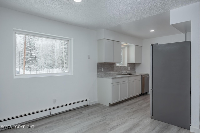 kitchen with a baseboard heating unit, light countertops, light wood-style flooring, appliances with stainless steel finishes, and a sink